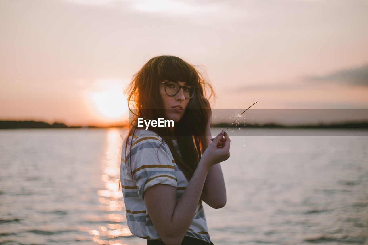 YOUNG WOMAN STANDING AGAINST SKY DURING SUNSET