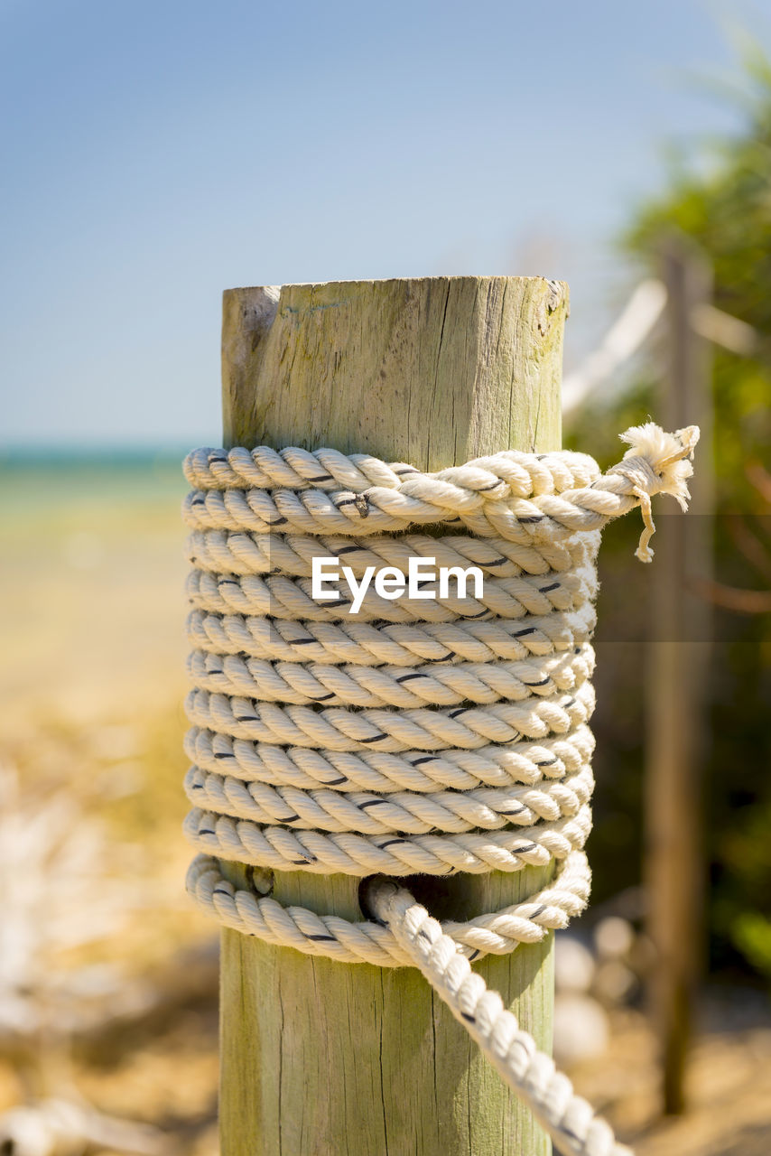 CLOSE-UP OF ROPE TIED ON WOODEN POST AT BEACH