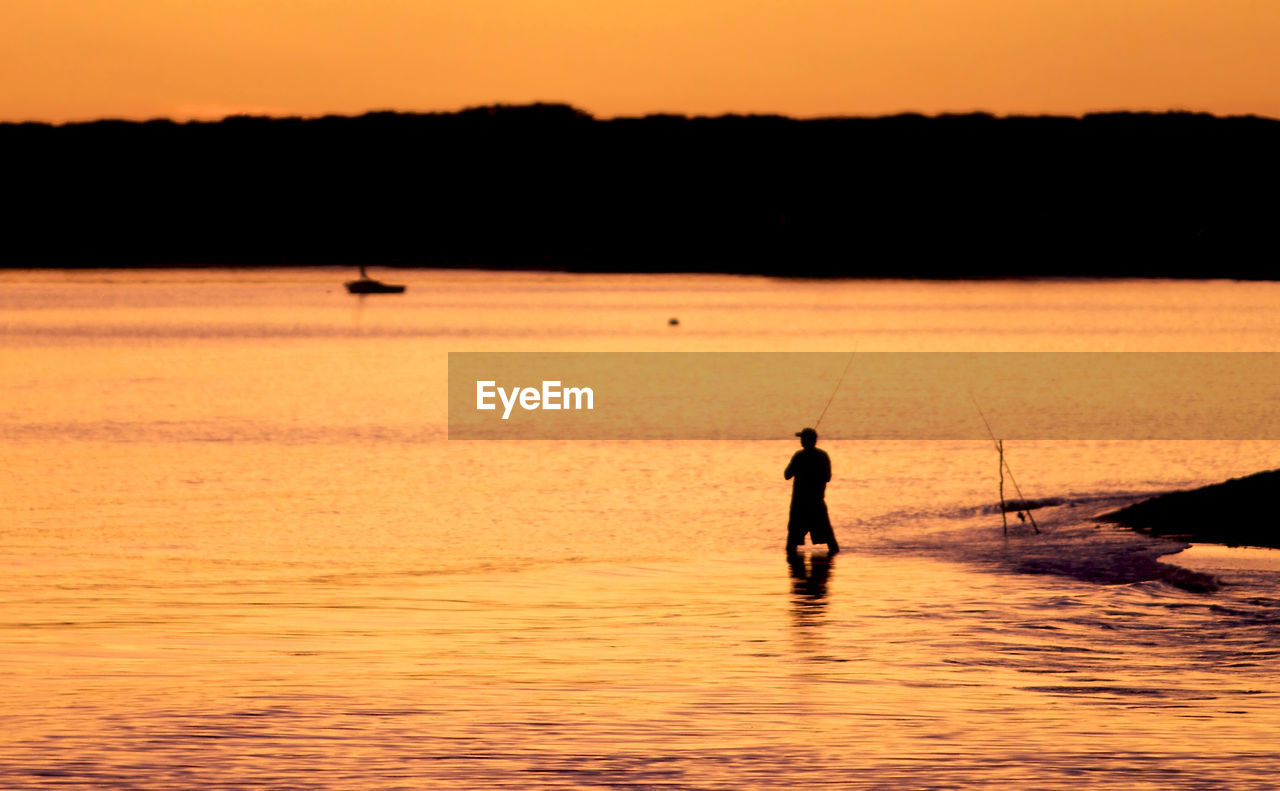 Rear view of silhouette man fishing in lake at sunset