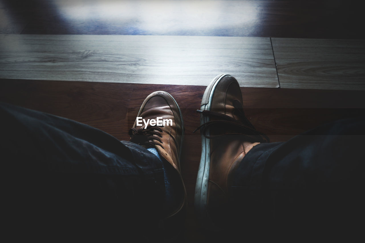 Low section of man wearing shoes on hardwood floor