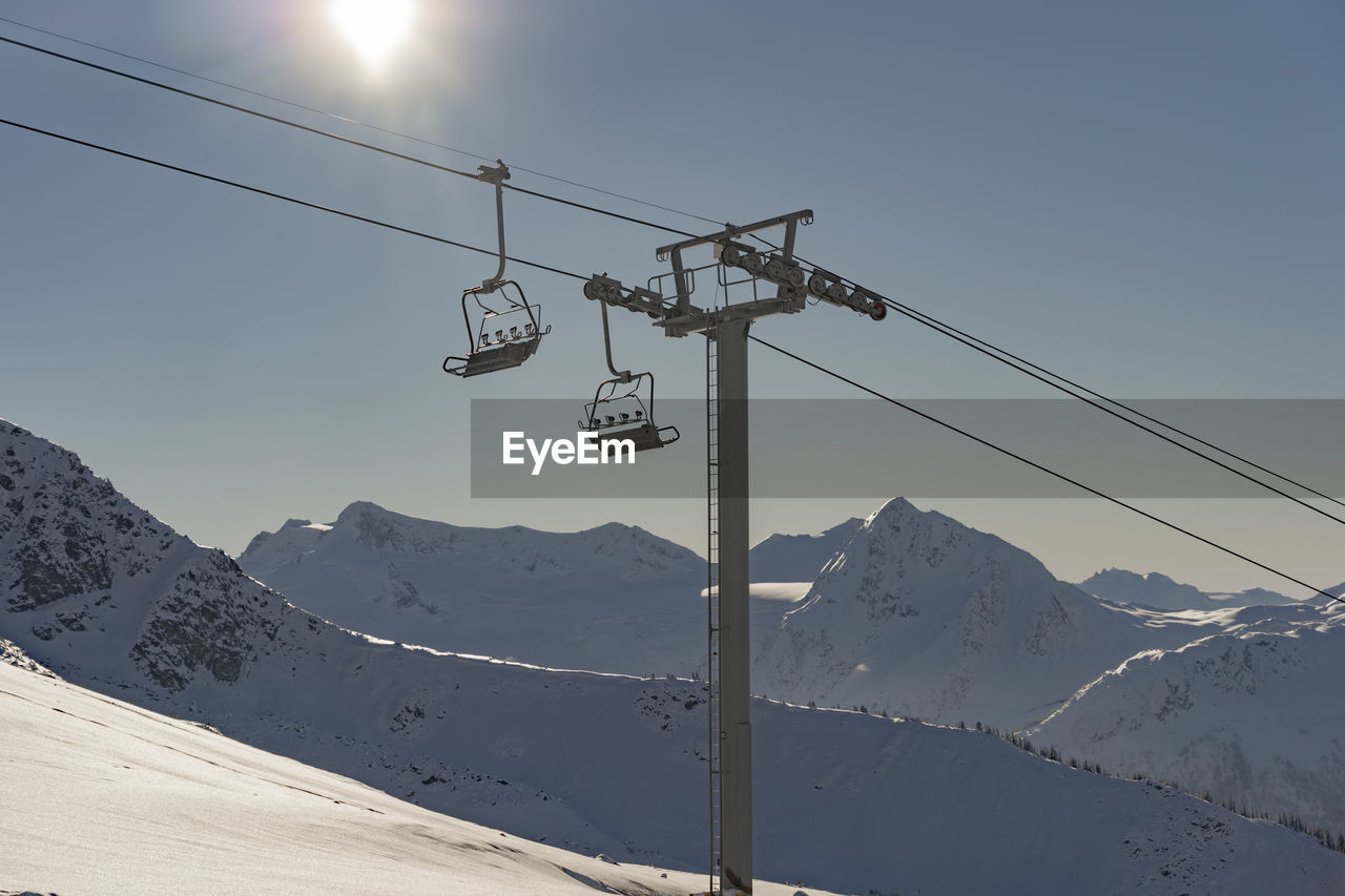 Low angle view of overhead cable car over snow covered mountain against sky