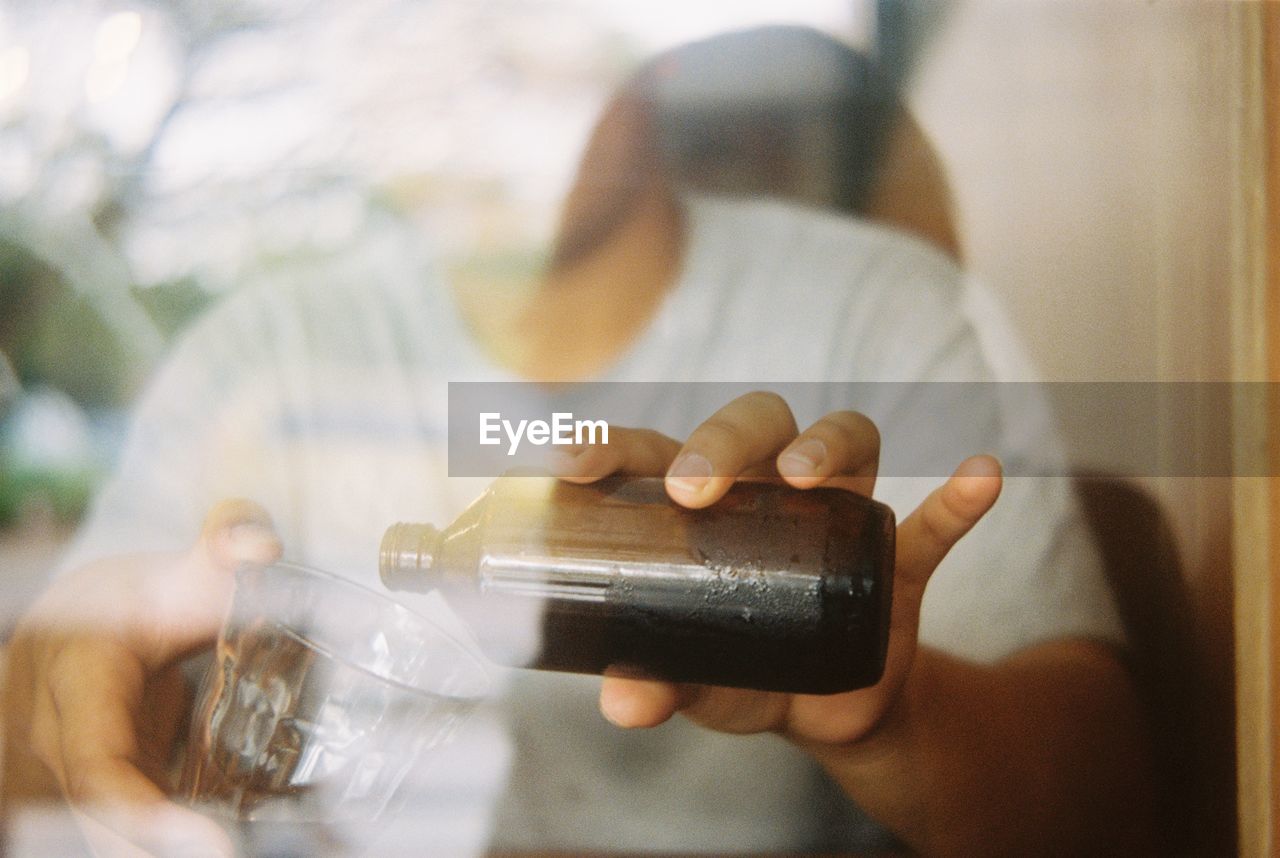 Midsection of man pouring cold brew in glass seen from window