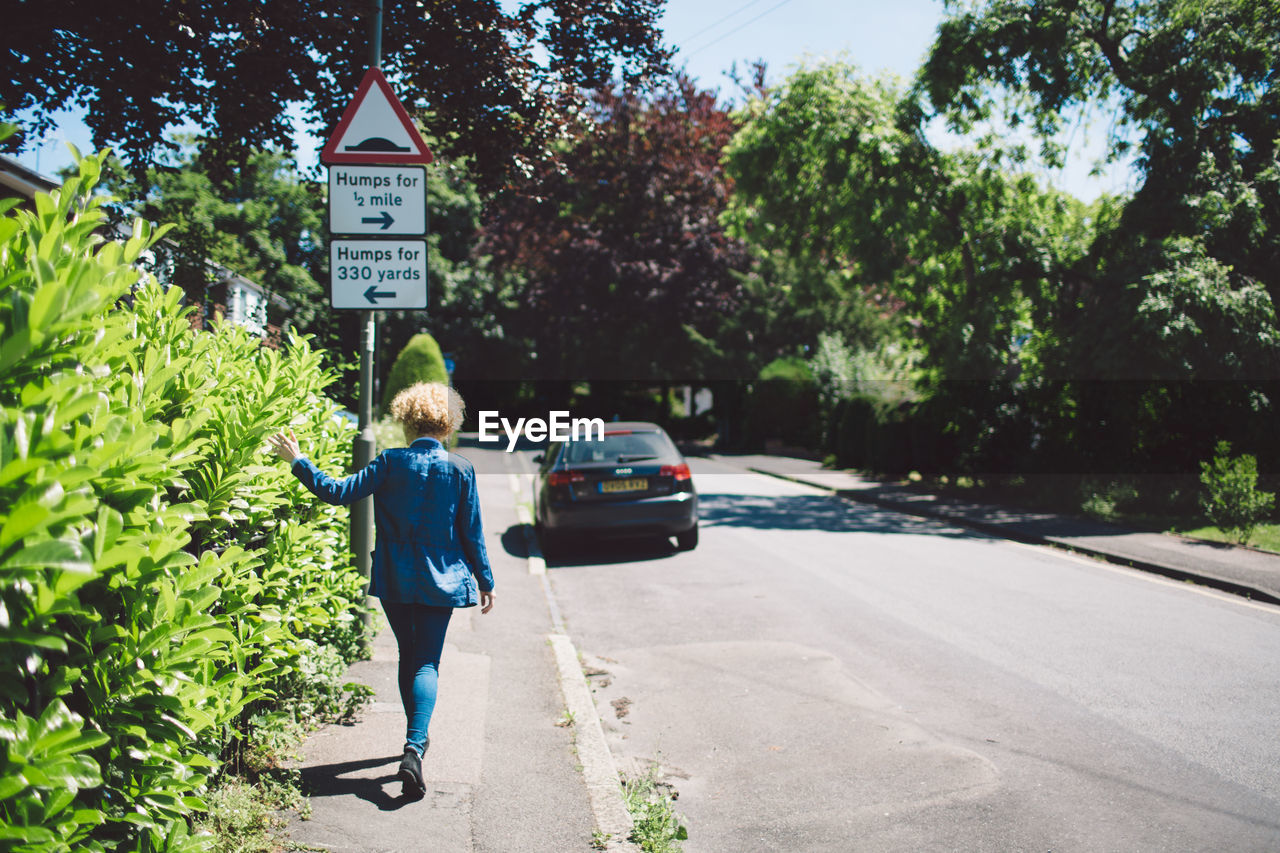 REAR VIEW OF A MAN WALKING ON ROAD