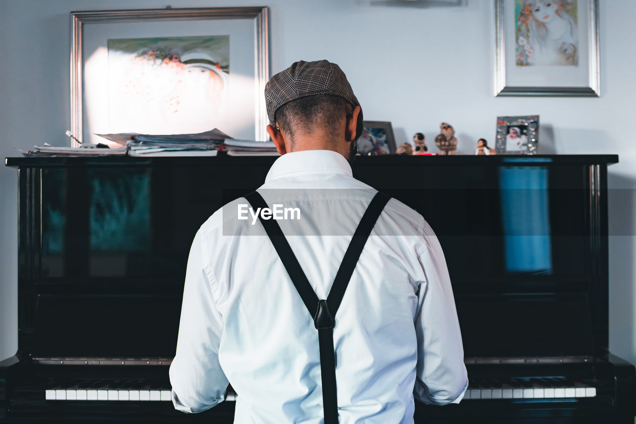 Rear view of man playing piano while sitting at home