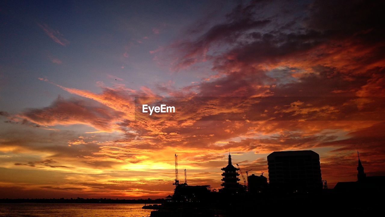 Silhouette of city against cloudy sky during sunset