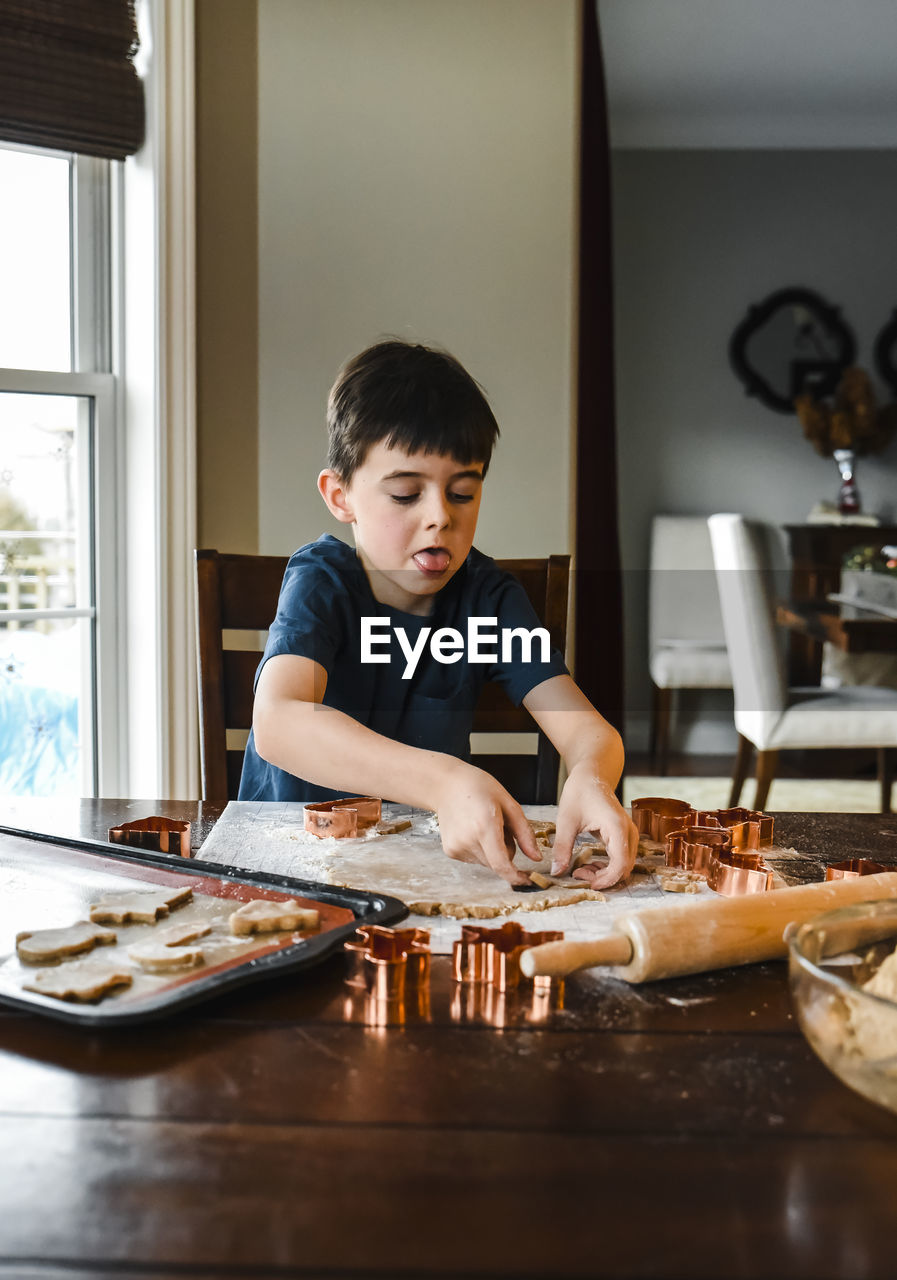 Young boy making cookies with cookie cutters at the table.