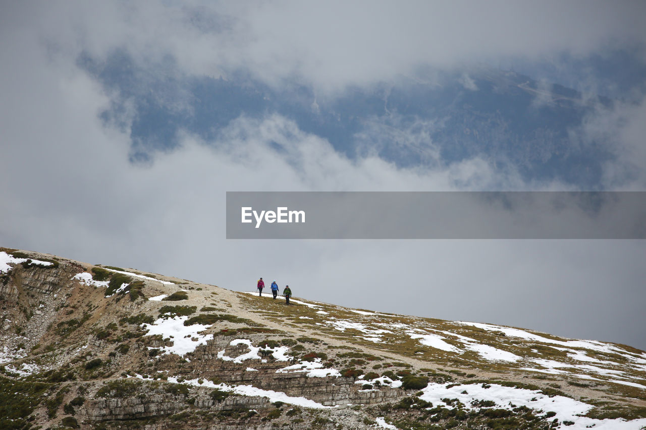 Hikers walking on snow covered mountain against sky