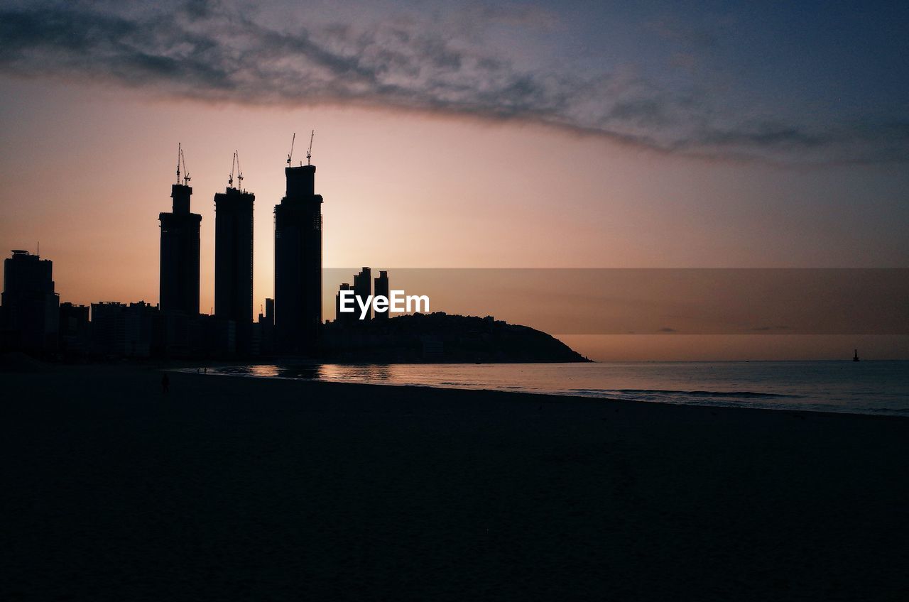 Silhouette of buildings by sea during sunset