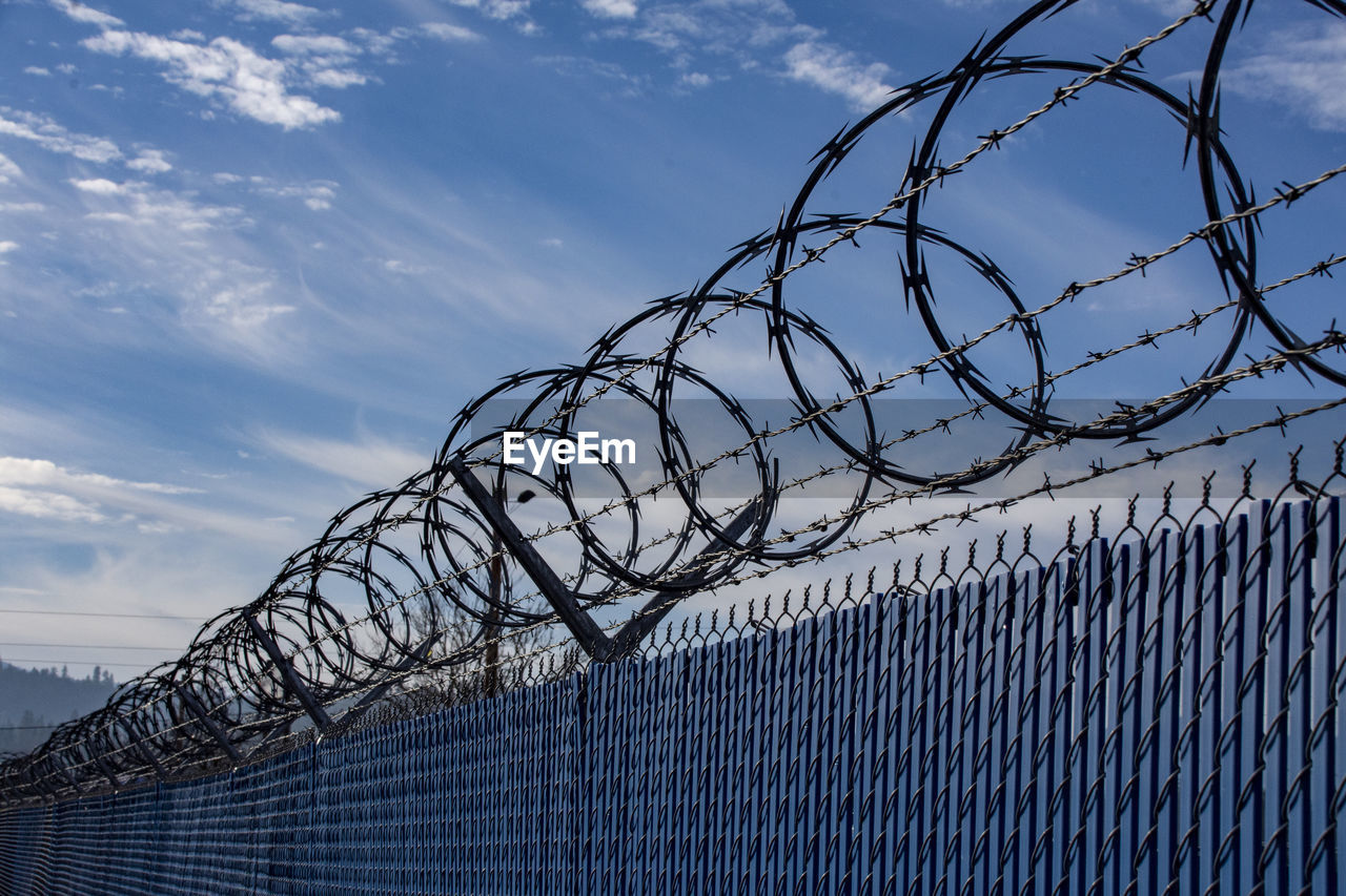 LOW ANGLE VIEW OF BARBED WIRE FENCE AGAINST CLOUDY SKY