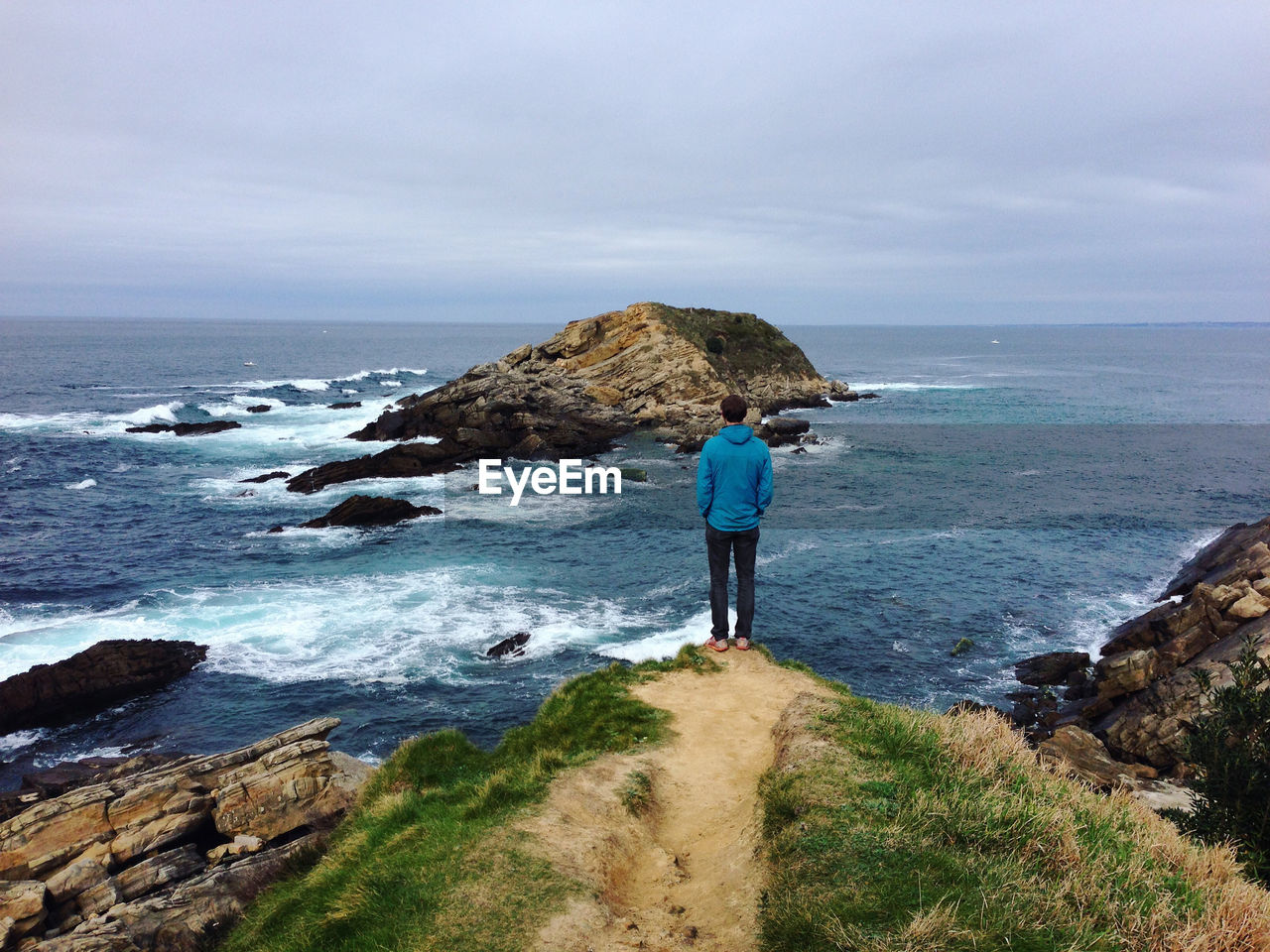 Rear view of man standing on cliff by sea against sky