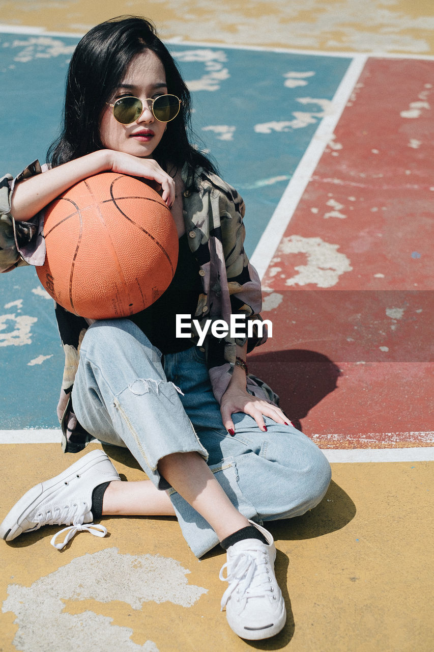 Smiling young woman with basketball sitting on court