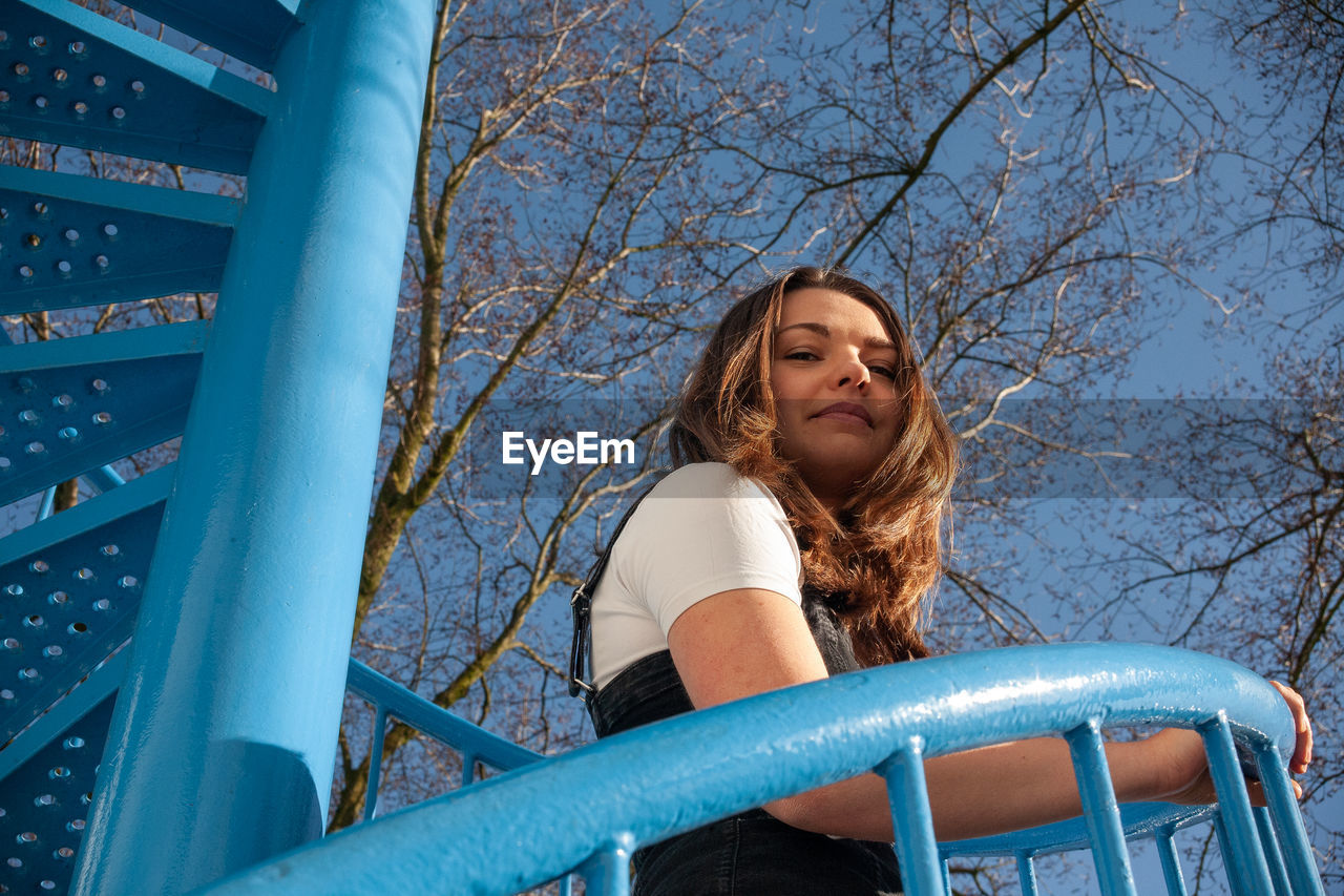 Low angle view of woman against trees against blue sky