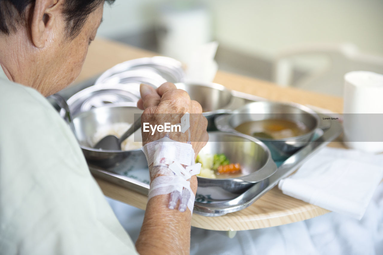 Senior asian patient woman in hospital eating lunch on tray, focus on hand with injection plaster.