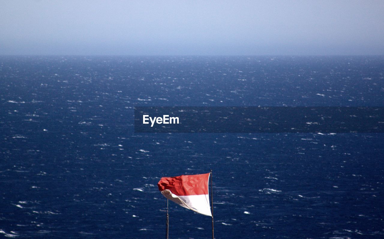 Waving flag by sea against sky