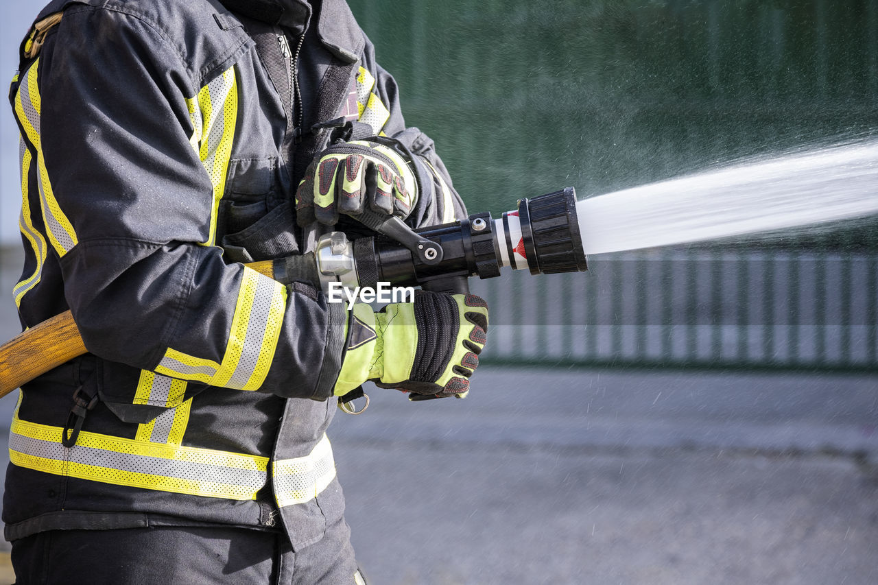 Midsection of firefighter holding fire hose outdoors