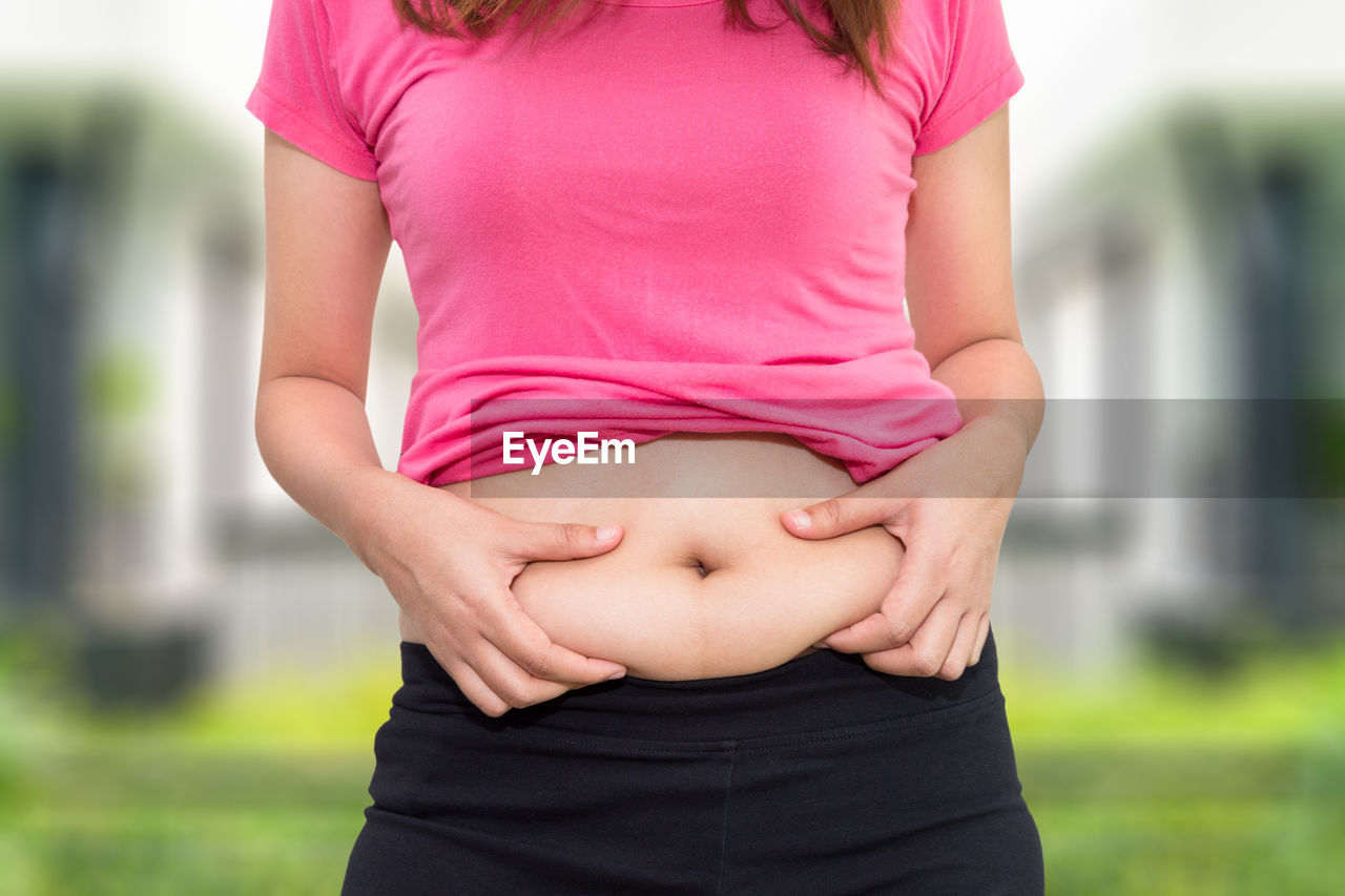 Midsection of woman pinching her belly outdoors