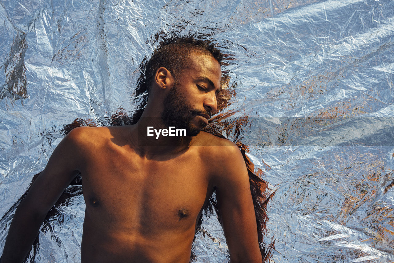 Shirtless man sleeping while lying on silver aluminum foil