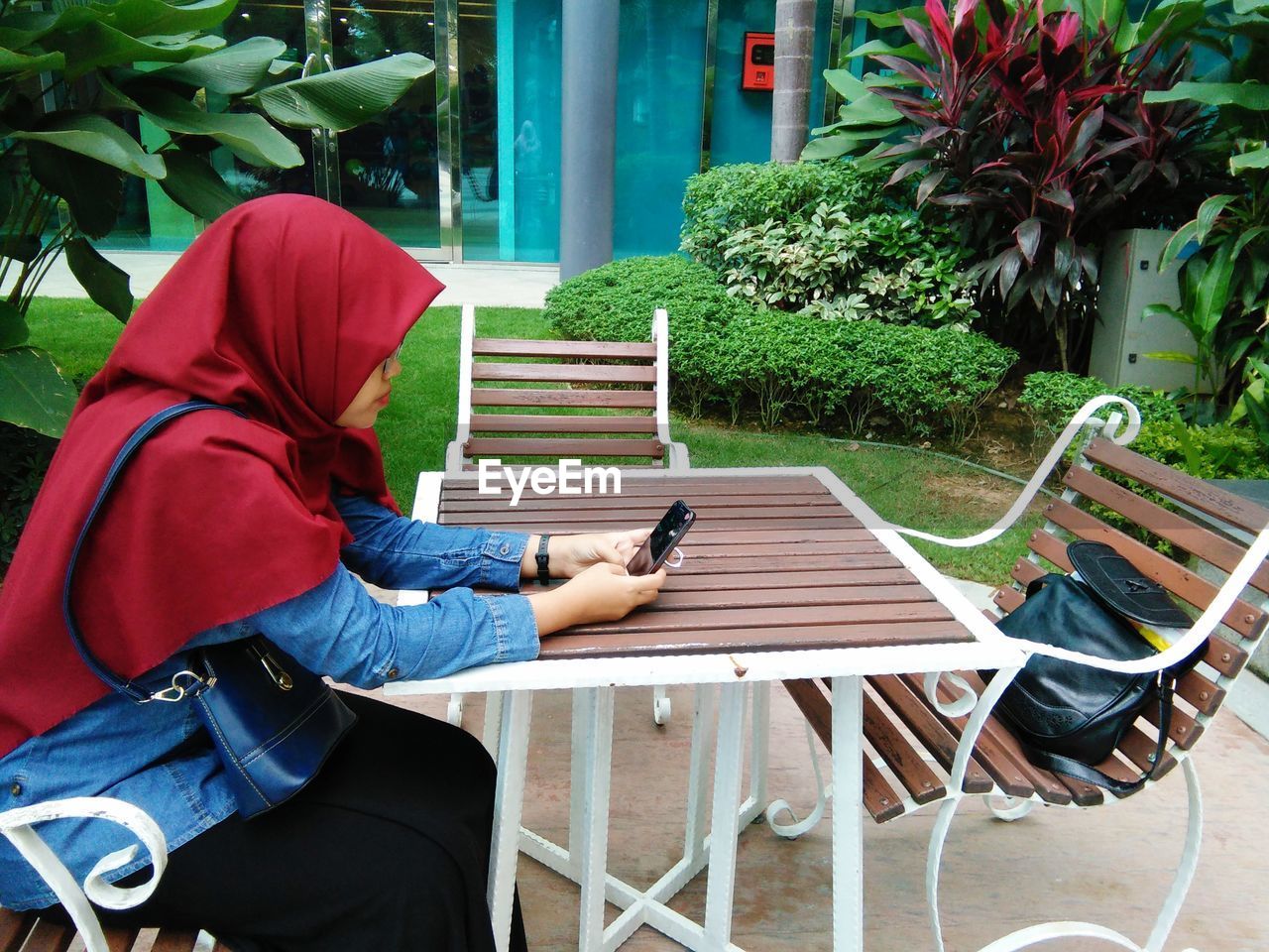 Side view of woman wearing hijab using smart phone while sitting outdoors