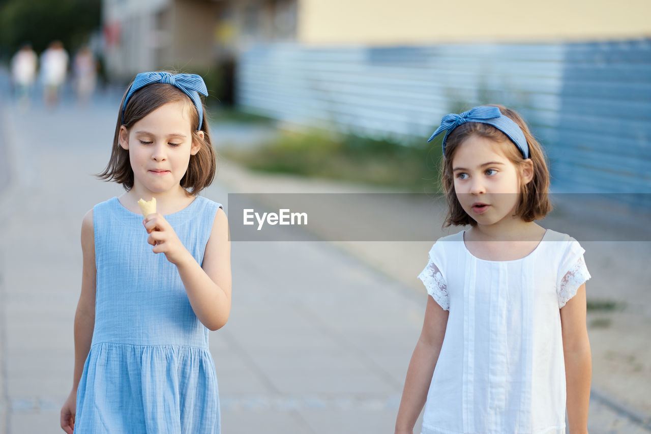 Girl eating ice cream while standing with friend on footpath