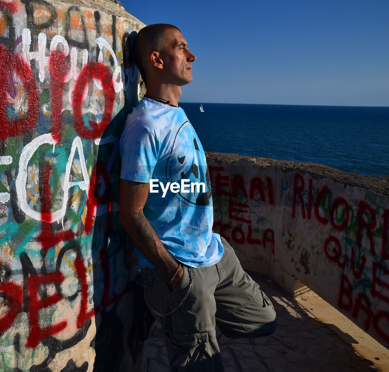 SIDE VIEW OF YOUNG MAN STANDING AGAINST WALL