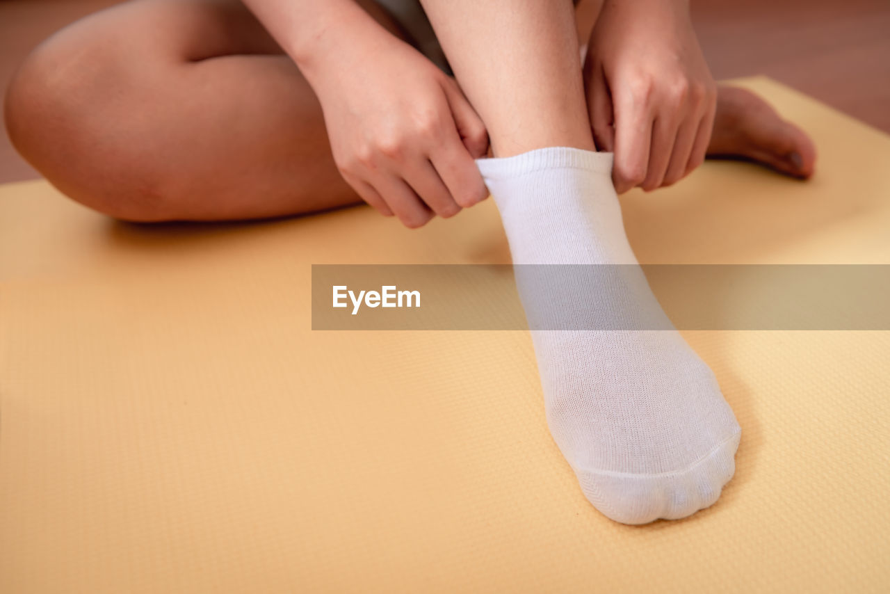 Low section of woman wearing sock while sitting on exercise mat