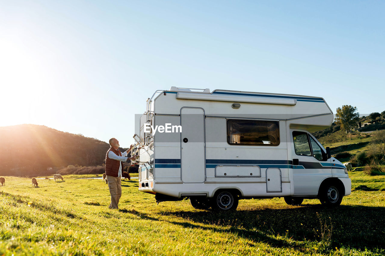 Side view of distant male traveler using metal folding step on rv car parked on field during road trip in countryside