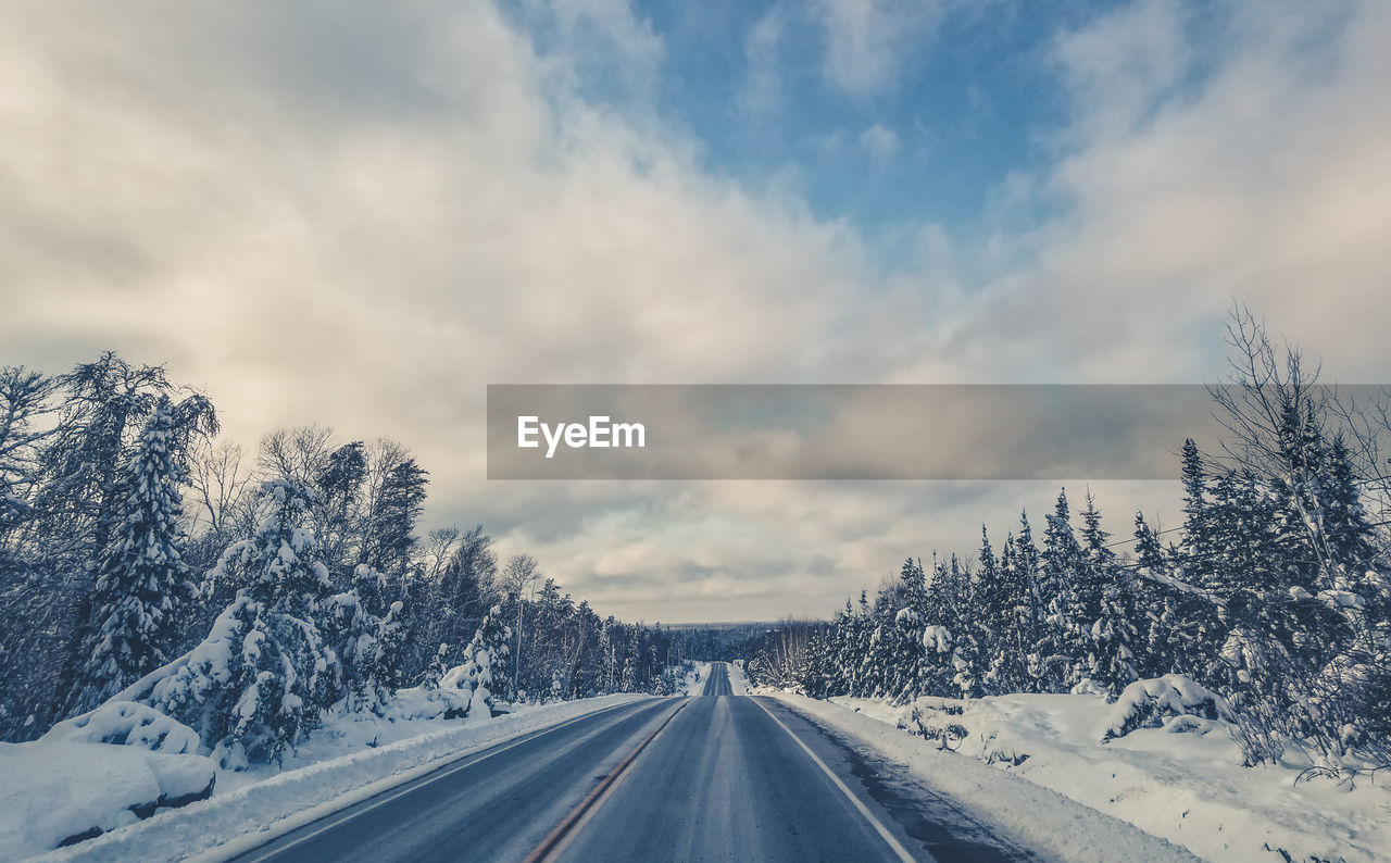 Road amidst snow covered landscape against sky