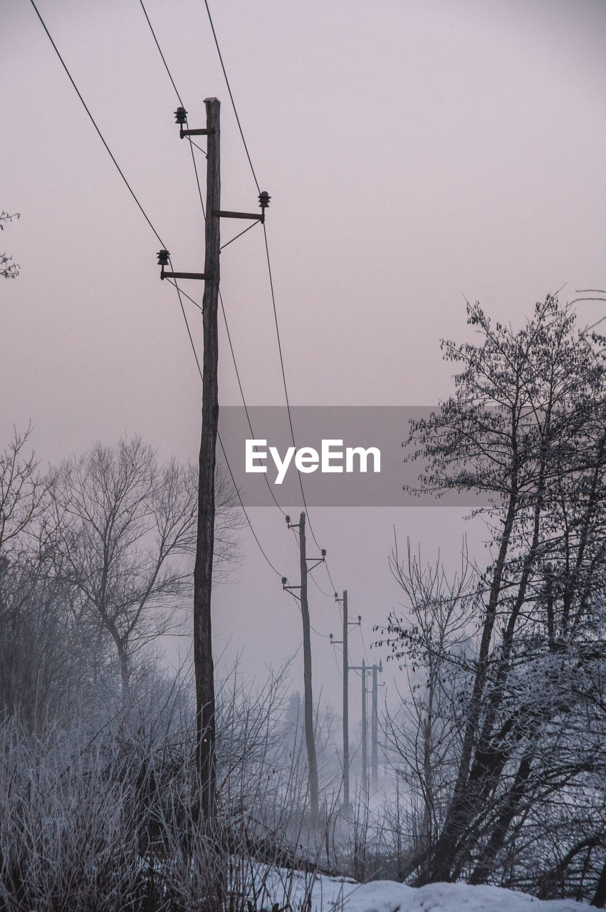 Old wooden electricity pylon in misty winter landscape