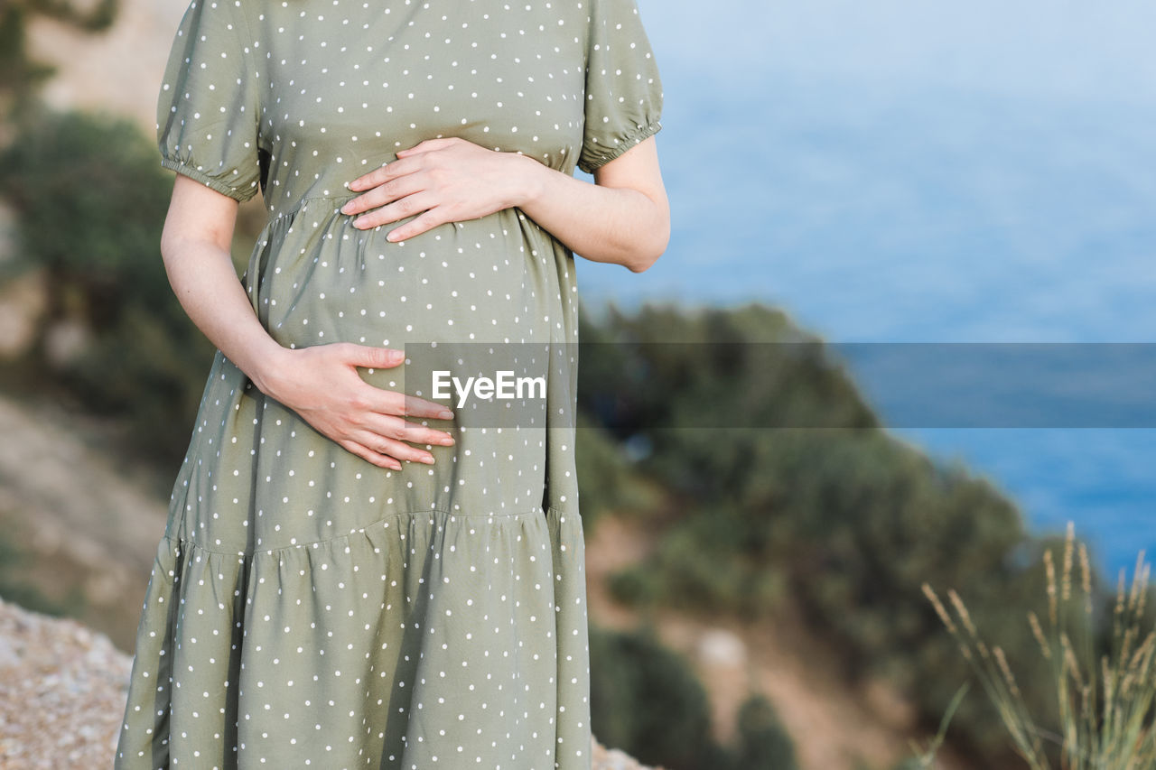Pregnant woman wearing dress posing outdoors over nature background closeup. motherhood. maternity. 