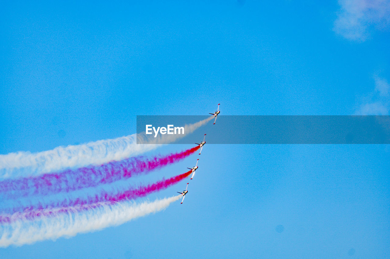 Low angle view of airplanes flying against blue sky
