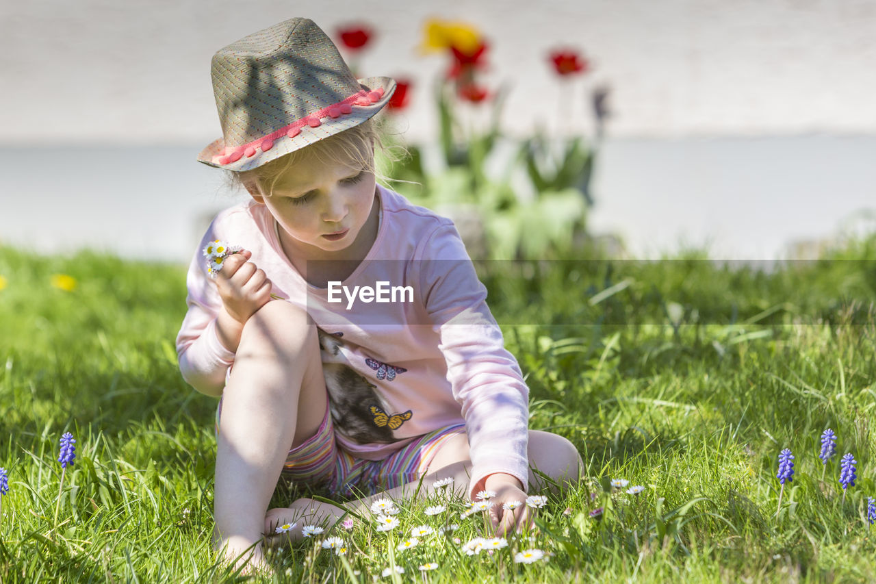 Girl picking flowers while sitting on grassy field