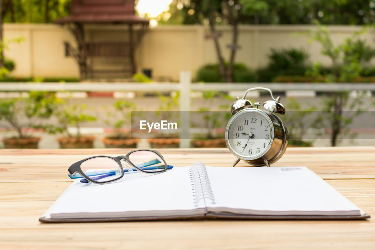 Close-up of open book with alarm clock and eyeglasses on table