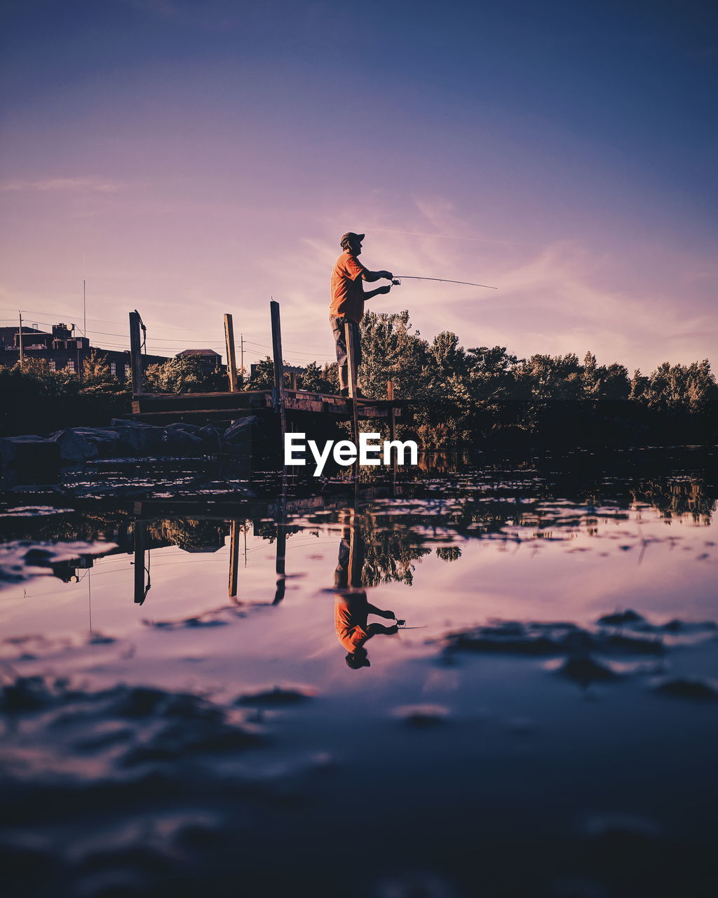 REFLECTION OF MAN ON LAKE AGAINST SKY DURING SUNSET