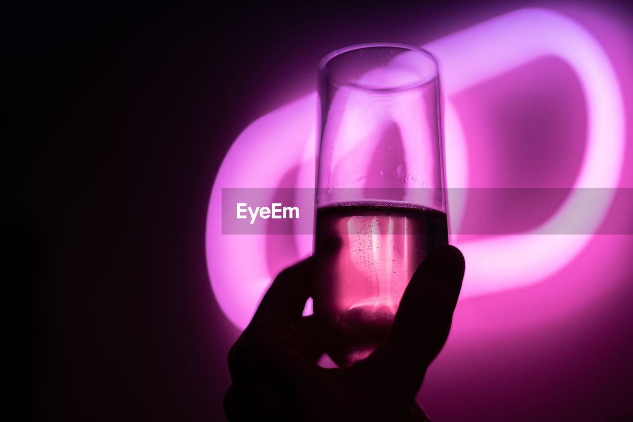 Close-up of hand holding glass against black and pink background