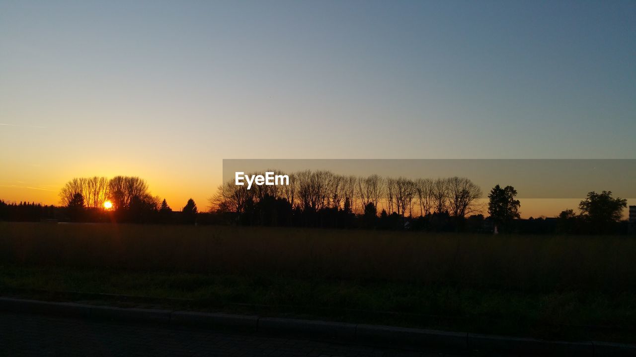 SCENIC VIEW OF SILHOUETTE FIELD AGAINST CLEAR SKY AT SUNSET