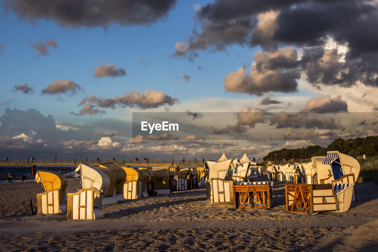 Hooded beach chairs on sand against sky