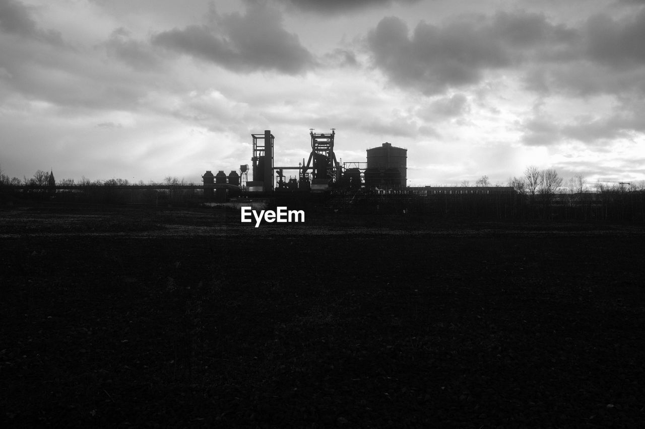 sky, horizon, cloud, darkness, industry, architecture, built structure, black and white, environment, building exterior, factory, skyline, monochrome photography, nature, monochrome, power generation, landscape, tower, no people, dusk, business finance and industry, outdoors, tree, fossil fuel, oil industry