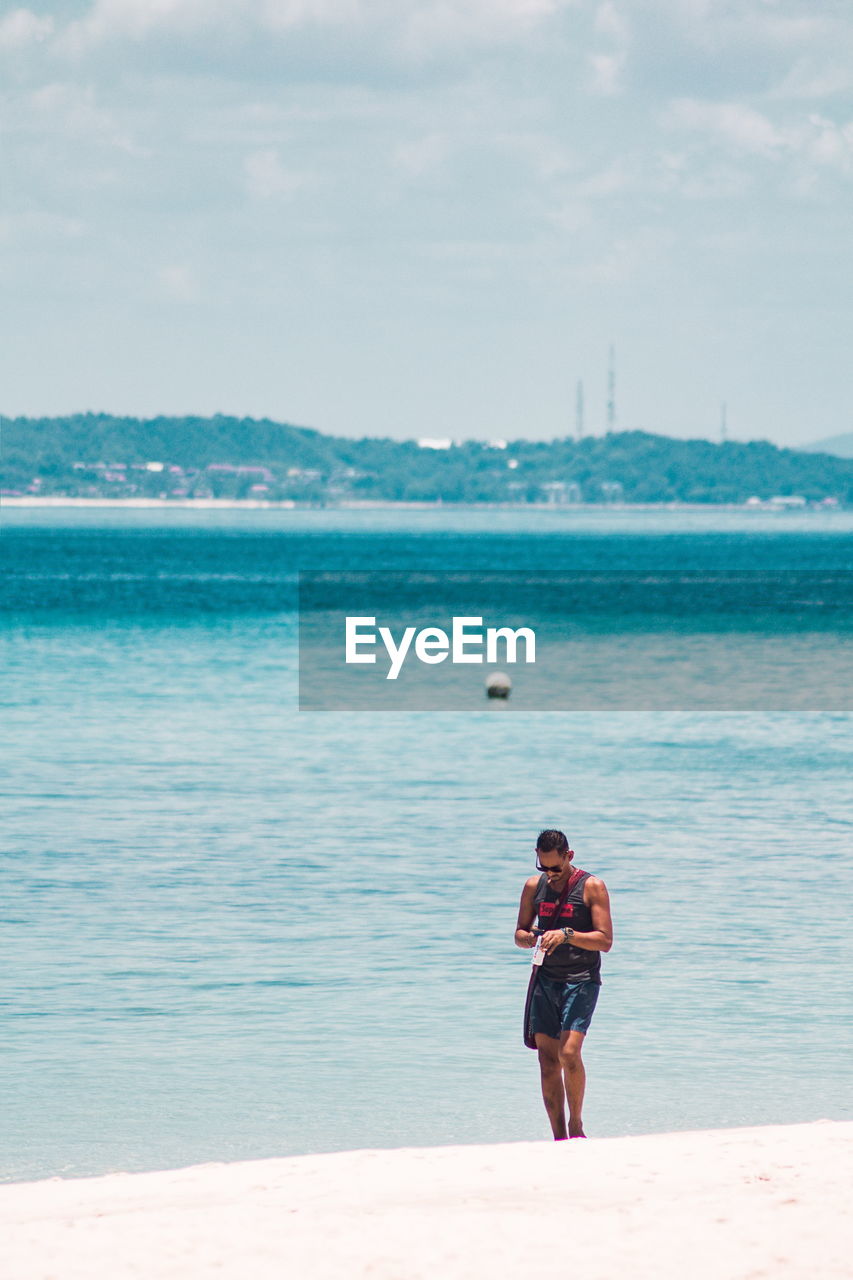 FULL LENGTH OF SHIRTLESS MAN STANDING ON BEACH