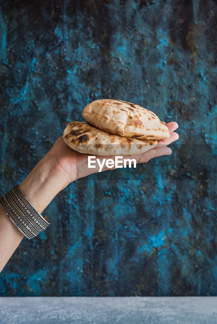 Cropped hand of woman holding flatbread against wall