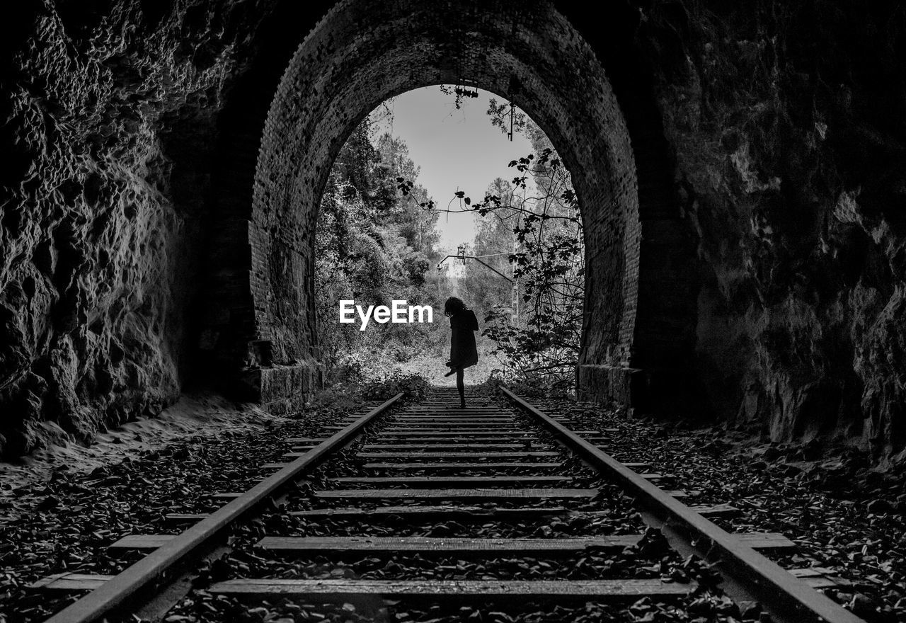 Rear view of so man standing on railroad tracks in tunnel