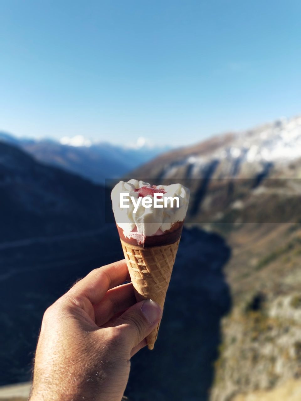 Cropped hand of man holding ice cream against mountain