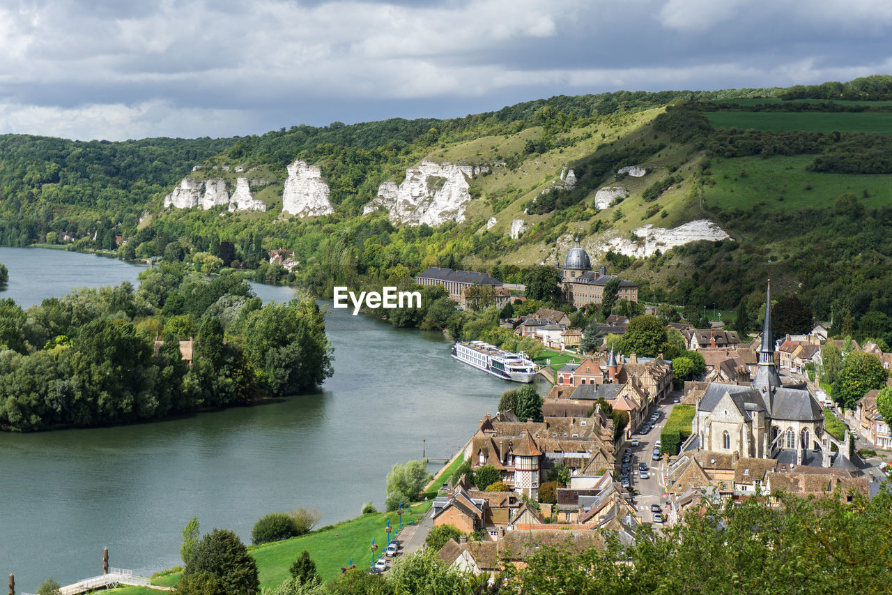 Townscape by river against cloudy sky