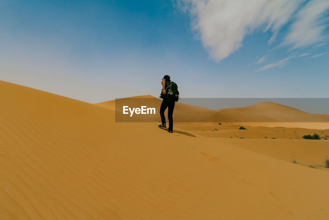 Full length man standing on sand dune in desert against sky