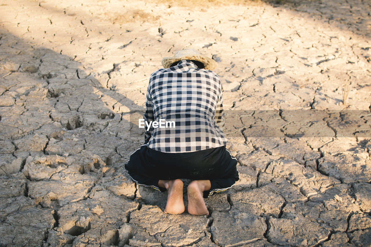 Rear view of person kneeling on cracked field