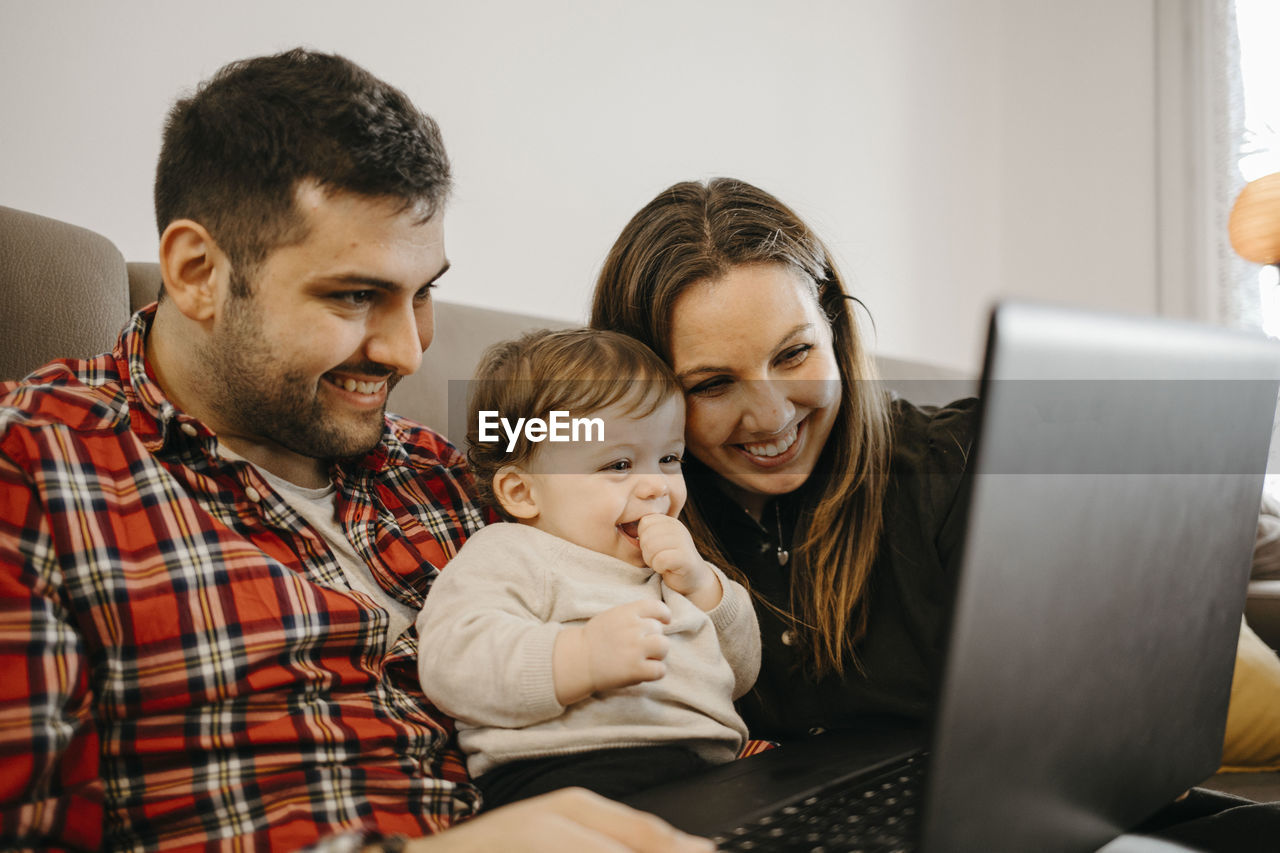 Happy mother and father with son during video call on laptop sitting in living room