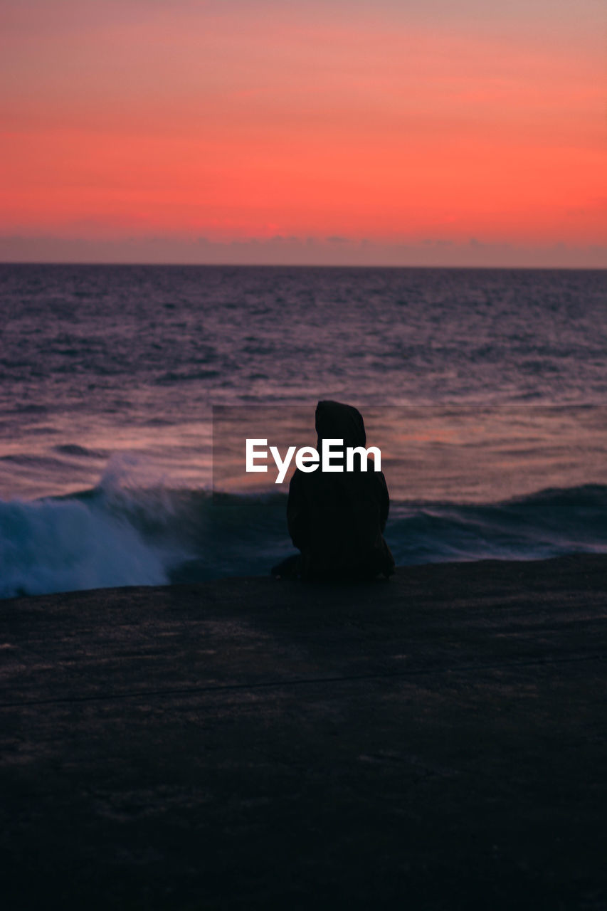 Rear view of man sitting on pier over sea during sunset