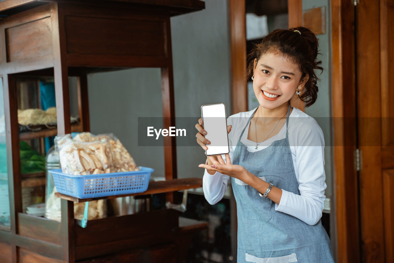 portrait of smiling young woman holding food in kitchen