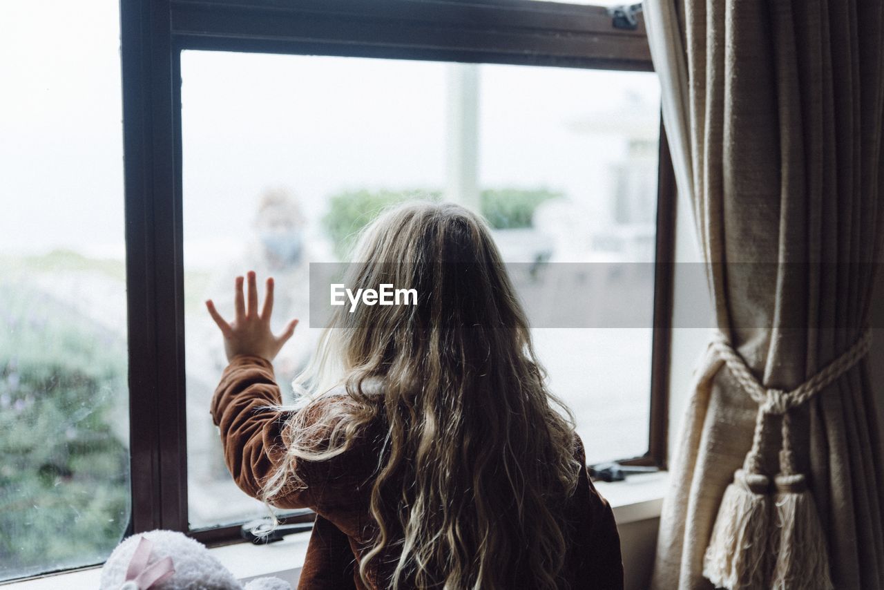 Rear view of girl looking through window at home