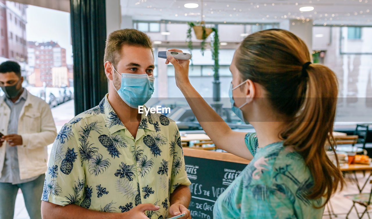 Woman checking temperature of customers wearing mask in restaurant