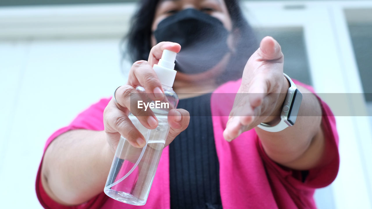 A woman wearing black mask is spraying hand sanitiser